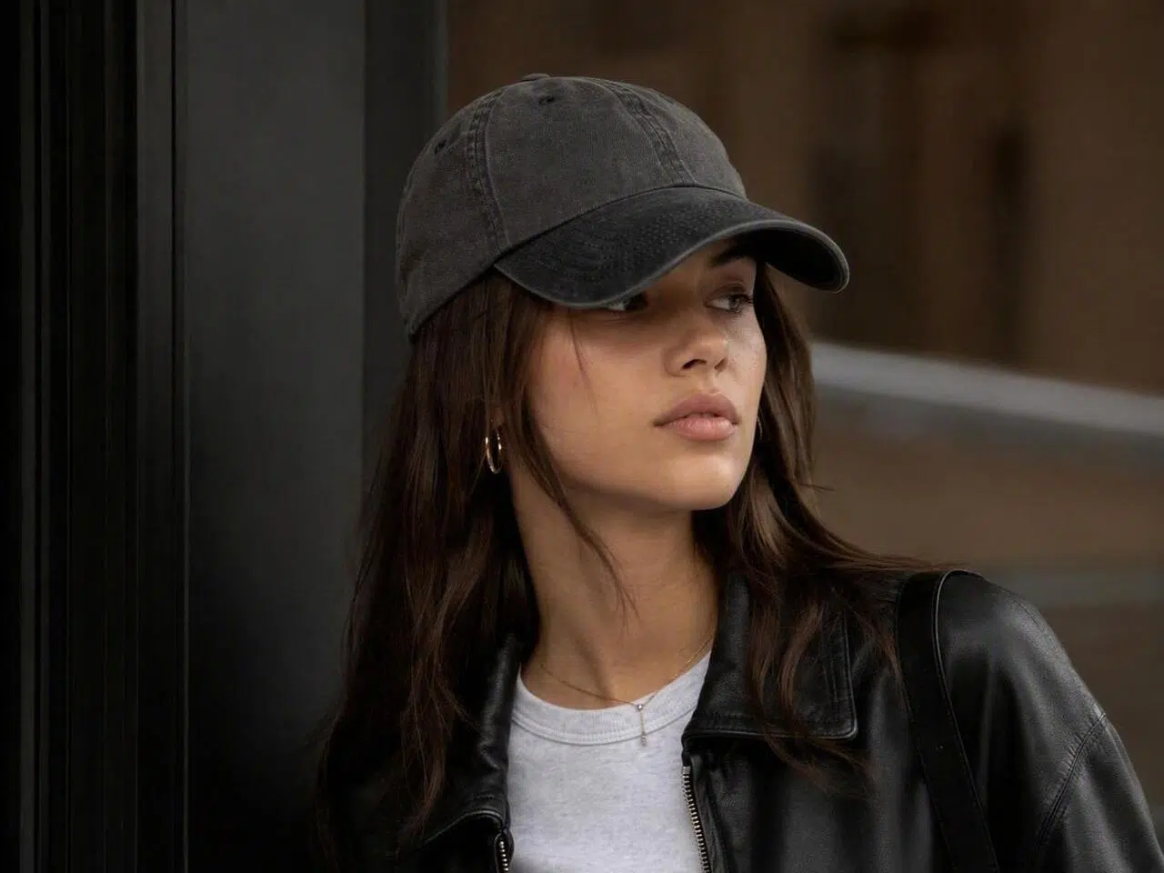 Primer plano de una modelo de pie, con una gorra de béisbol negra y una chamarra de cuero.